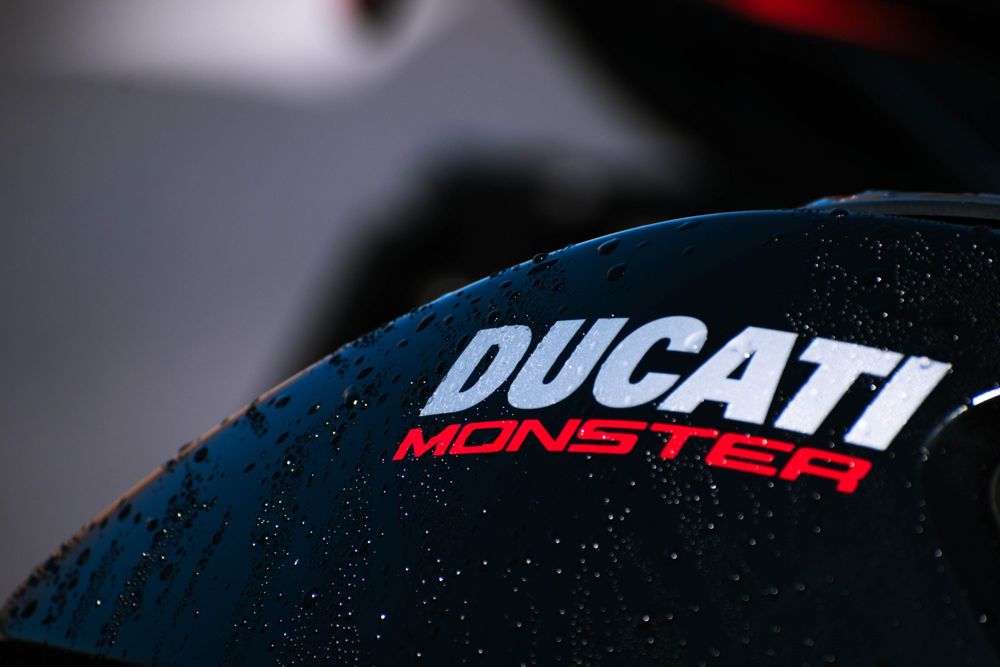 Ducati Monster lettering on a black fuel tank in the rain