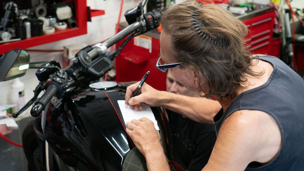Pinstriping being drawn by hand on a black Ducati fuel tank