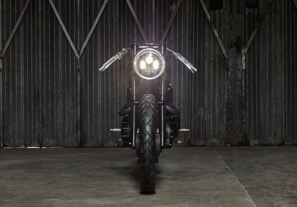 Up Yours Copper Triumph from the front, headlight on, in a warehouse