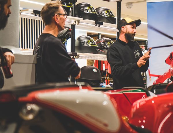 Two men talking beside a classic Ducati among the helmet displays