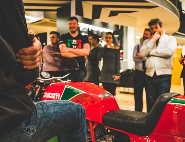 Rider sitting on a classic red and green Ducati as guests watch