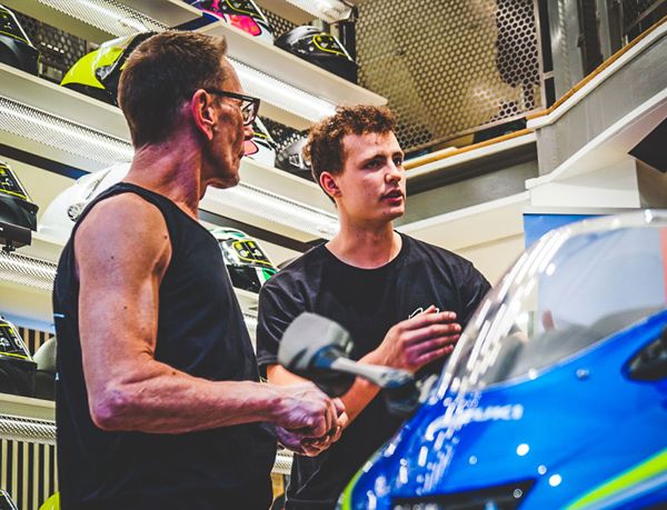 Two RPM team members talking beside a blue motorcycle