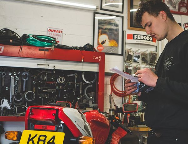Mechanic reading notes beside a Ducati in the workshop