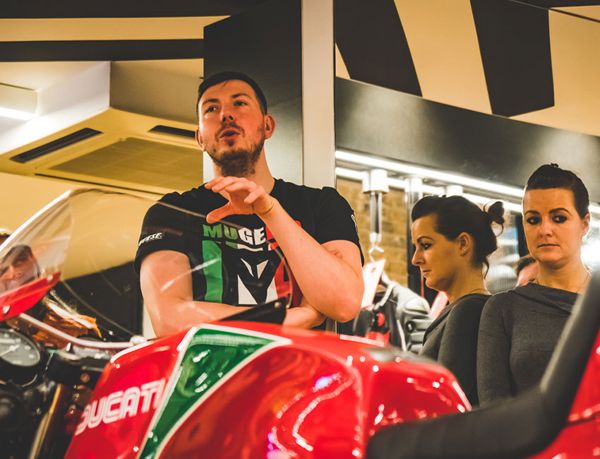 Speaker addressing guests beside a classic red and green Ducati