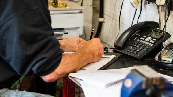 Mechanic writing up a job sheet beside the workshop telephone