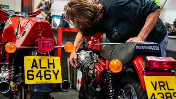 Mechanic working on a red Moto Guzzi beside another classic Guzzi