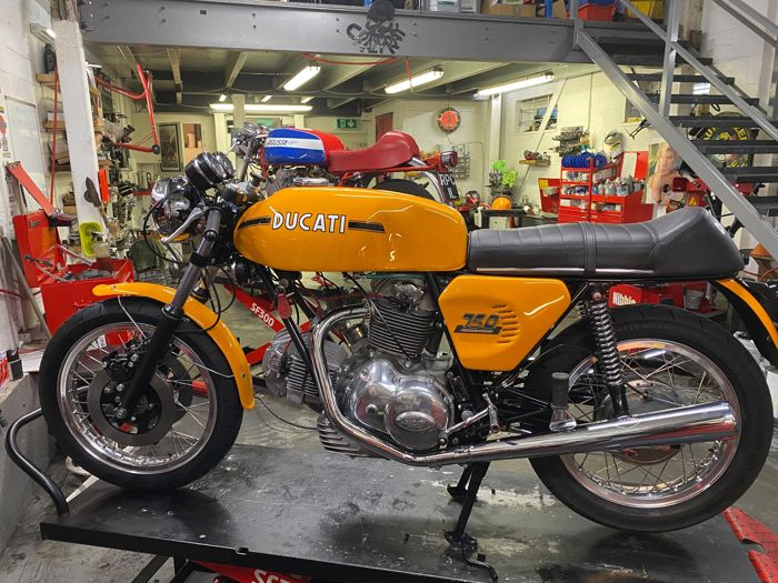 Yellow and black 1975 Ducati 750 Sport on a lift in the RPM workshop
